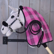 A Hobby Horse LarDen "Set Harmony Pink" stick toy in gray is mounted on a wooden wall, dressed in a pink and black plaid stable blanket with a black halter and matching coiled lead rope on its side.