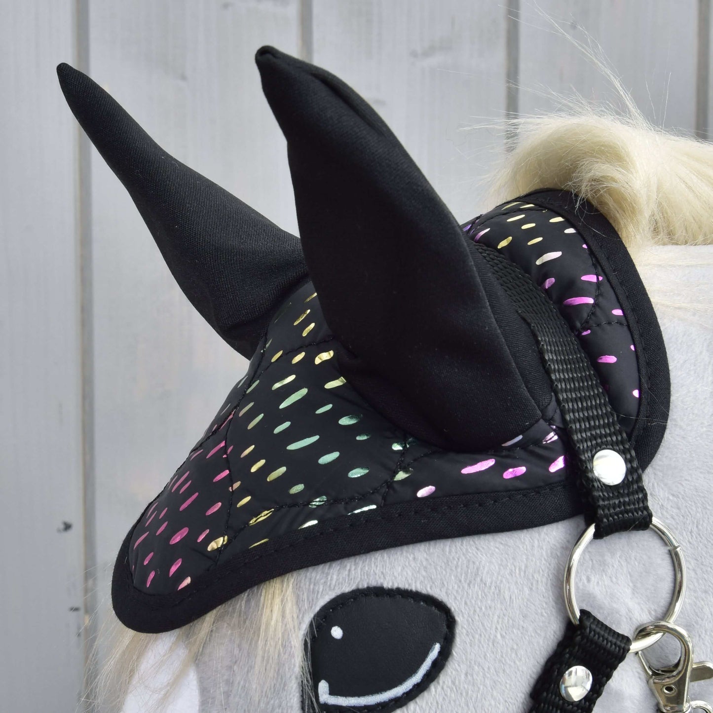 Ensemble Rêveur de Hobby Horse LarDen, gros plan sur un Hobby Horse avec corps blanc, bonnet d'oreilles noir à pois réfléchissants colorés, œil souriant en feutrine et bride, sur fond de panneaux de bois clair.