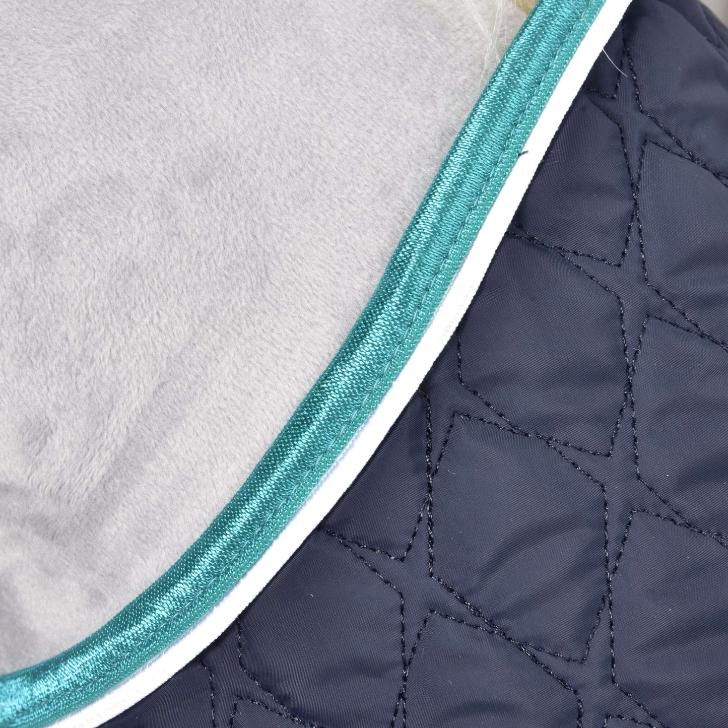 Gros plan sur la couverture Ensemble Suprême Turquoise de Hobby Horse LarDen, avec tissu bleu foncé matelassé à surpiqûres géométriques, bordure turquoise et passepoil blanc, idéale pour protéger votre cheval.