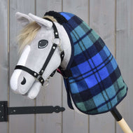 The Hobby Horse LarDen hobby horse features a gray fabric head, black bridle, light mane, painted-on eye and nostril, and wears the Stable Blanket Perth in blue-and-green plaid. It stands against a wooden background.