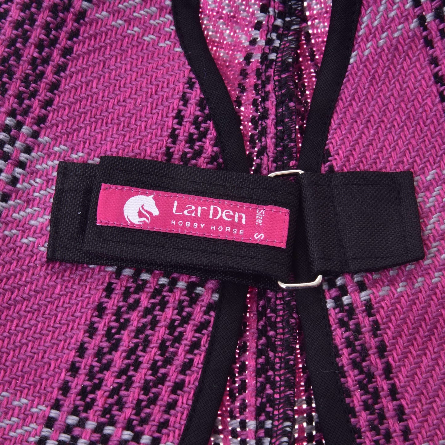 Gros plan sur la Couverture d'écurie rose de Hobby Horse LarDen, avec sangle noire et étiquette rose portant l'inscription « LarDen HOBBY HORSE S size » et un logo tête de cheval. La couverture est tissée en rose, noir et blanc.