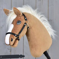 Hobby Horse Star mit schwarzem Halfter von Hobby Horse LarDen mit karamellfarbenem Fell, weißer Mähne und schwarzem Zaumzeug vor grauem Holz-Hintergrund.