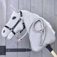Hobby Horse LarDen Hobby Horse - Führstrick Tizian in Grau mit schwarzem Zaumzeug, weißer Mähne und hellem Holzstab lehnt an einer grauen Wand. Ein aufgerollter Führstrick – ideal als Spielzubehör – hängt an seinem Hals.