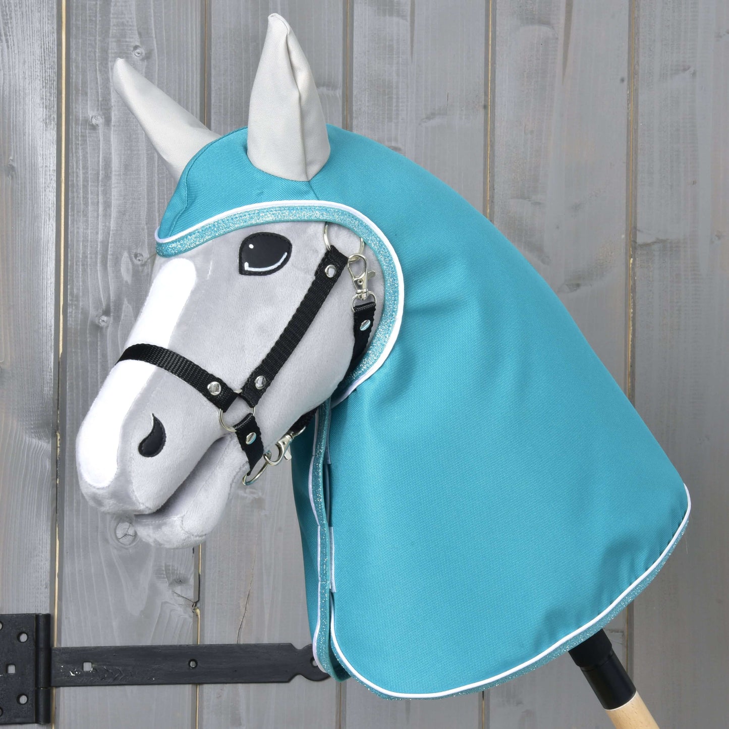 Imperméable turquoise de Hobby Horse LarDen avec Hobby Horse gris, bride noire et capuche style imperméable turquoise, avec visage de forme réaliste aux détails noirs et blancs, sur fond en bois clair.