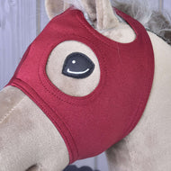 Nahaufnahme eines beigen Hobby Horse von Hobby Horse LarDen mit Maske ohne Ohren Velvet in rotem Samt, die den Kopf bedeckt, mit gestickten Augen und sichtbarer flauschiger Mähne.