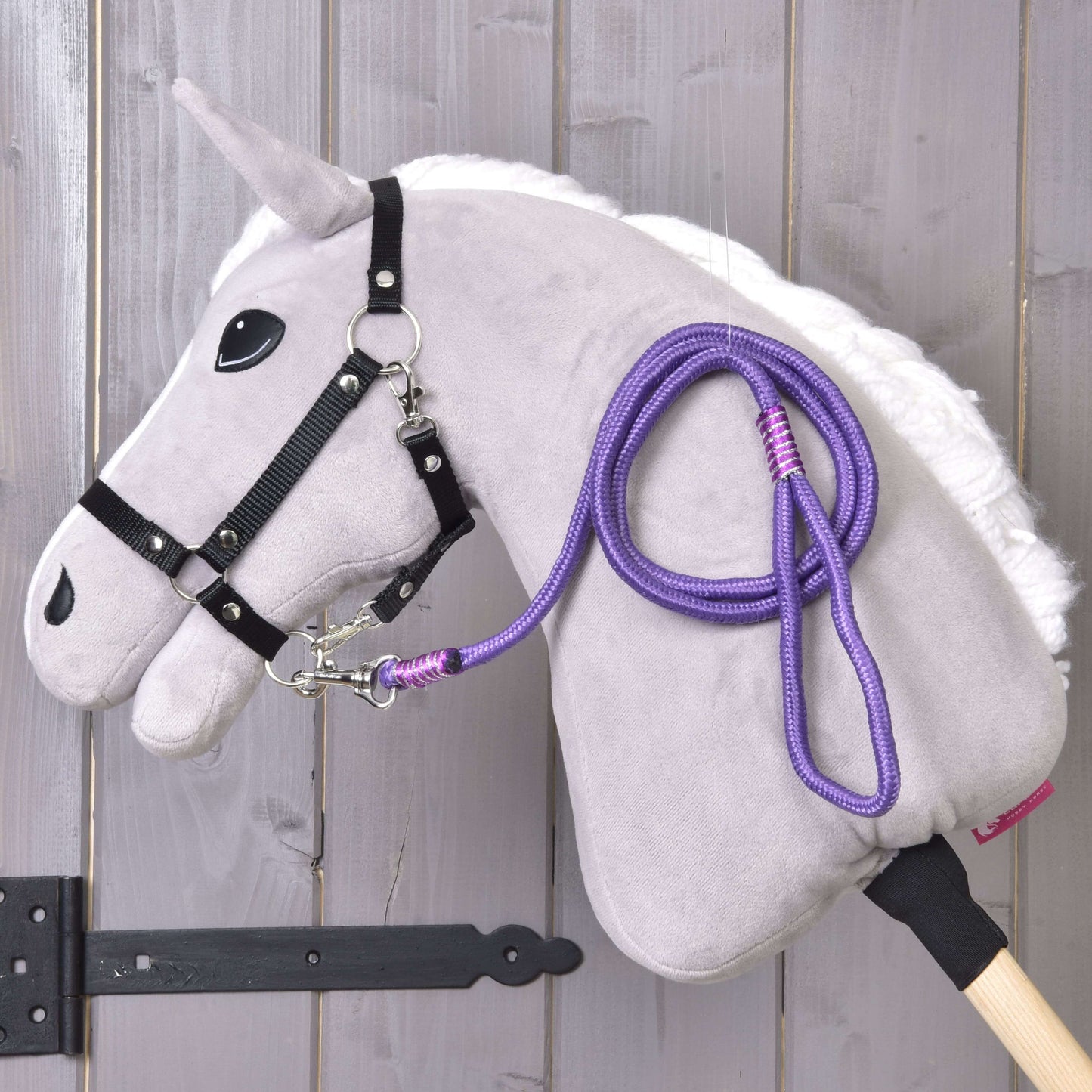 Hobby Horse - rayure corde Viola de Hobby Horse LarDen sur un Hobby Horse en peluche avec crinière blanche, bride noire, laisse en corde violette et bâton en bois, présenté devant un mur en bois clair.