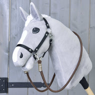 Zügel Vivaldi von Hobby Horse LarDen, braune handgefertigte Zügel aus Polypropylen, über ein graues Hobby Horse mit weißer Blesse, schwarzem Halfter für Hobby Horse und Holzstab vor grauem Holzgrund drapiert