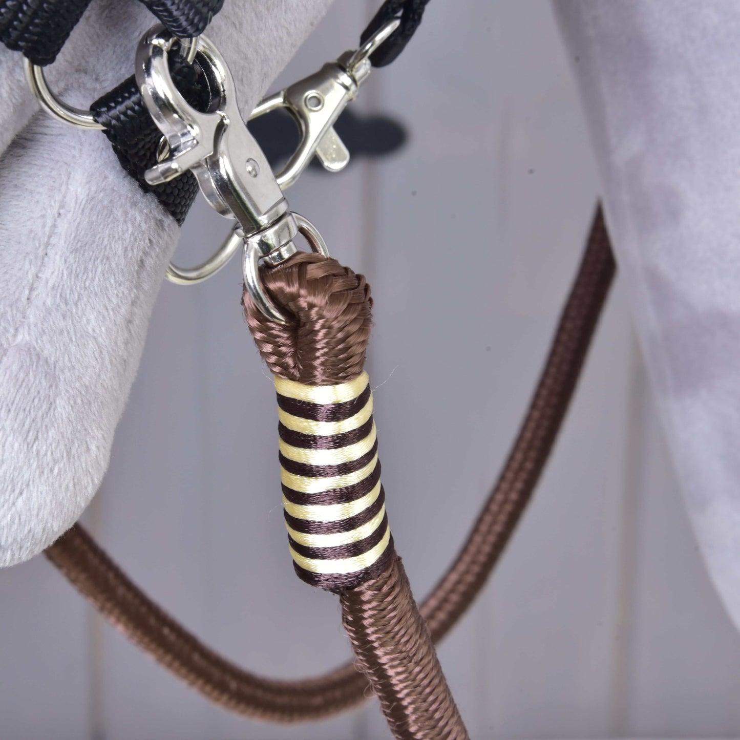 Gros plan sur un clip métallique fixant une corde en polypropylène marron avec enroulement décoratif or et noir à un tissu gris, faisant partie des rênes Vivaldi de Hobby Horse LarDen.