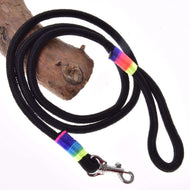 The Hobby Horse LarDen "Hobby Horse - Lead rope Rainbow" is a black rope leash with colorful pink, blue, green, and yellow sections near the handle and silver clip, coiled on wood and inspired by horse lead ropes.