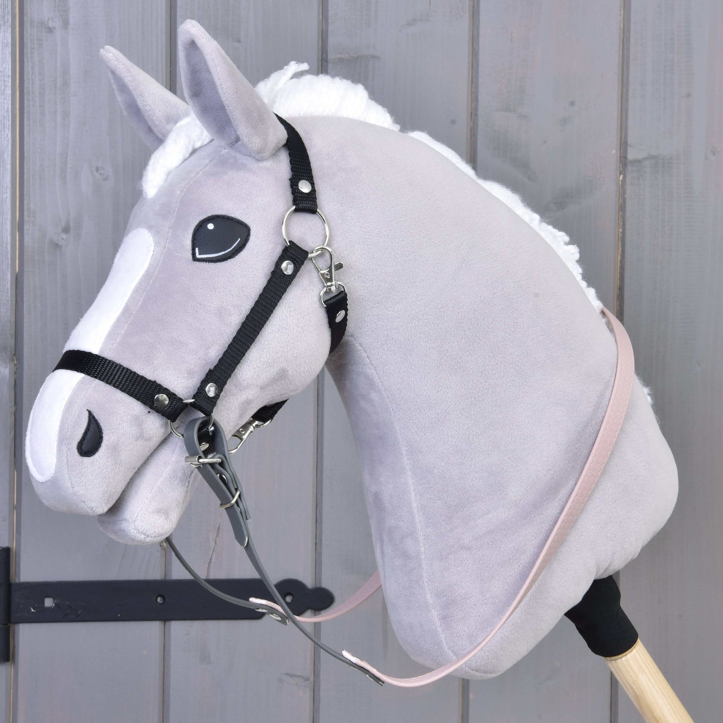 Nahaufnahme eines Hobby Horse LarDen mit hellgrauem Kopf, weißer Mähne und Gummierte Zügel - Dark Grey/pink, befestigt an einem cremefarbenen Stab vor Holzhintergrund.