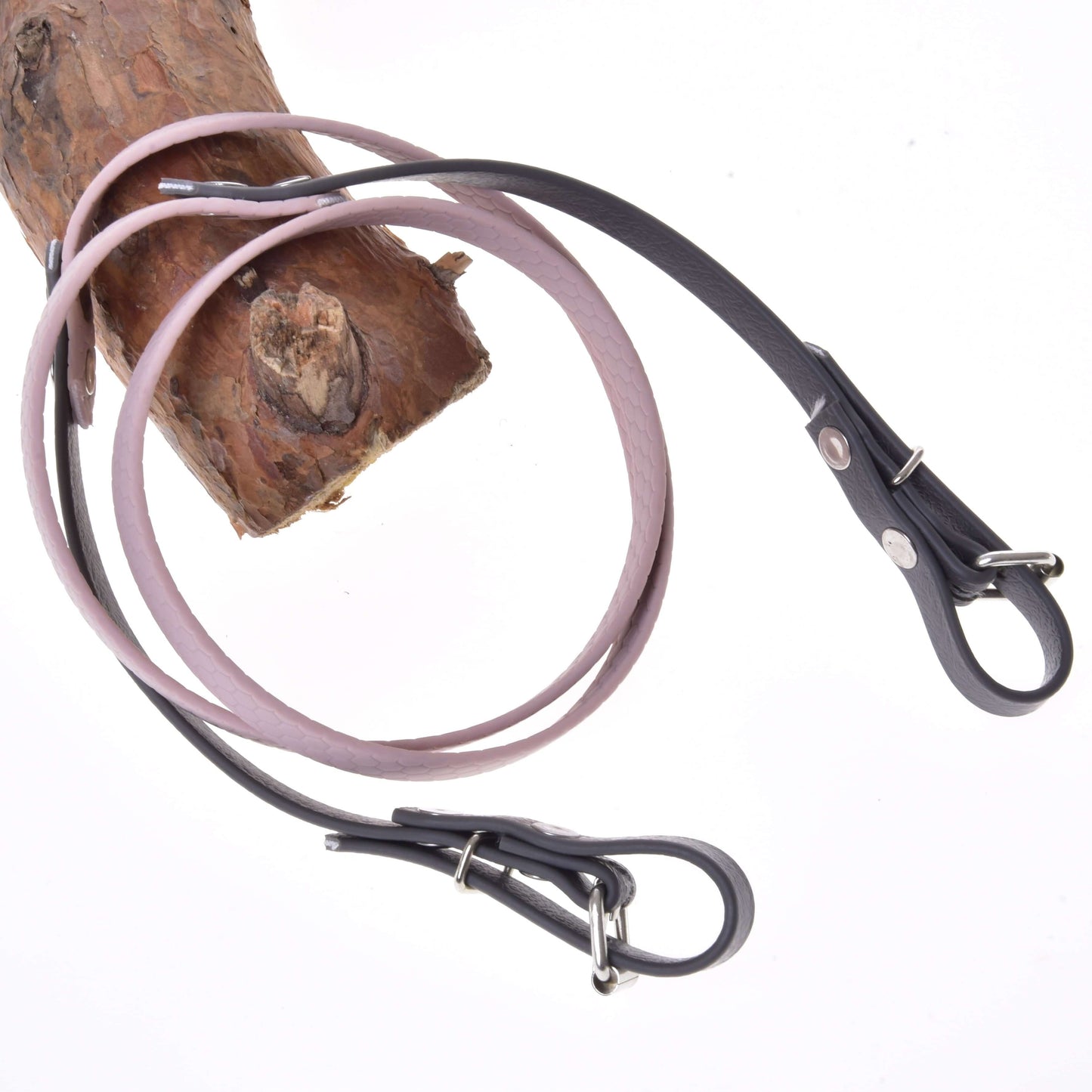 Ein hellbrauner Ast mit zwei Hobby Horse LarDen Gummierte Zügel - Dark Grey/pink, darum geschlungen, lederähnlichen Hundeleinen ähnlich, vor weißem Hintergrund.