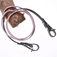 Rênes caoutchoutées Gris Foncé/Rose de Hobby Horse LarDen enroulées autour d'une branche en bois marron clair, ressemblant à des laisses en cuir pour chien, sur fond blanc.