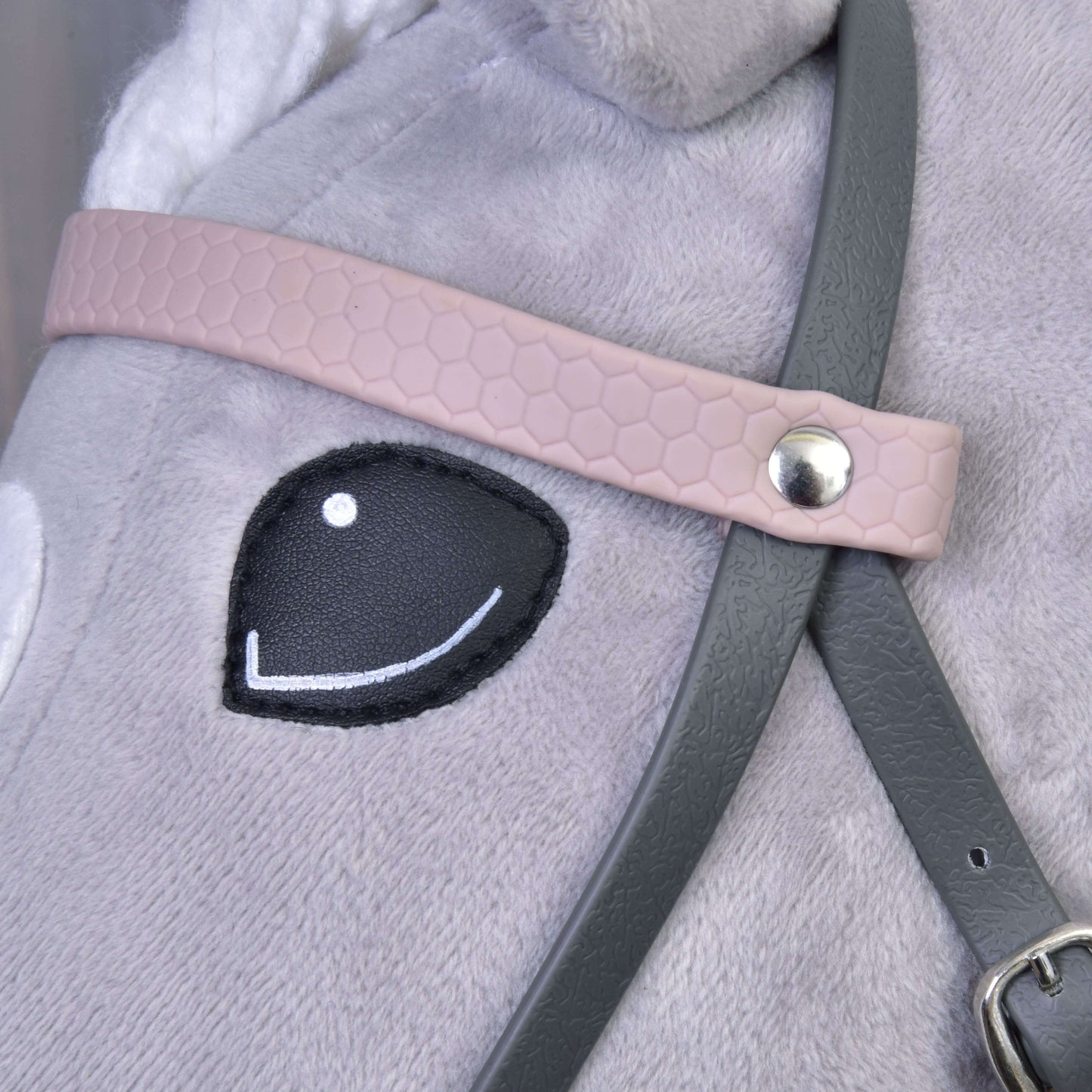 Nahaufnahme von Hobby Horse LarDen „Komplettes Kunstlederzaumzeug Grau mit Pink Stirnriemen“ auf einem Plüschpferd mit schwarzem gesticktem Auge und detaillierten Riemen, die mit einer Metallniete befestigt sind.