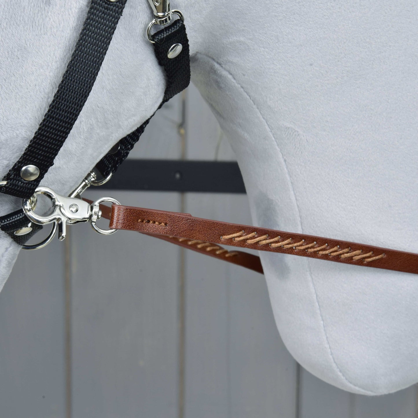 Gros plan sur une tête de cheval blanche avec bride et Rênes Western Fendues Marron Foncé de Hobby Horse LarDen, fixées par un mousqueton métallique, sur fond de panneaux en bois clair.