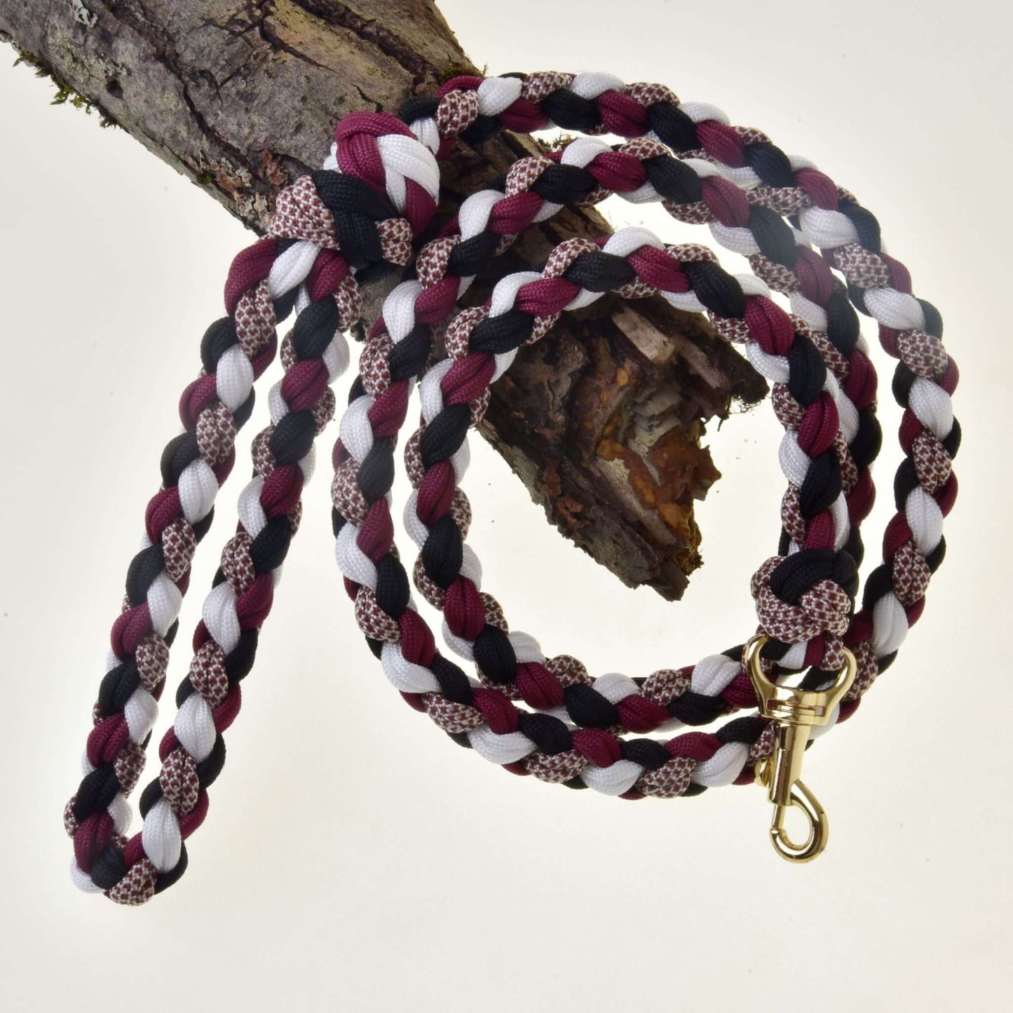 Hobby Horse - Cordelette tressée noir/blanc/bordeaux de Hobby Horse LarDen, en noir, blanc et bordeaux, suspendue enroulée sur une branche d’arbre, avec un mousqueton en métal doré à une extrémité.