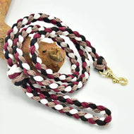 The Hobby Horse LarDen braided lead rope in black, white, and bordeaux with a brass clip is coiled neatly beside wood on a white background.