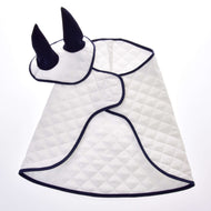 Set Thermo White (Ohrenkappe + Decke) von Hobby Horse LarDen enthält eine weiße gesteppte Decke mit dunkler Einfassung in Umhangform und eine passende Ohrenkappe mit zwei aufrechten schwarzen Hörnern.