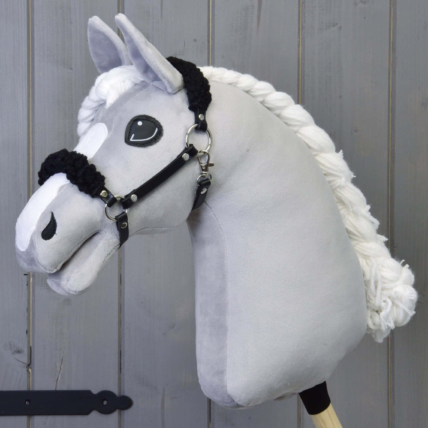 Licou noir avec fourrure noire - similicuir de Hobby Horse LarDen, présenté sur un Hobby Horse en peluche gris clair avec grand yeux brodés et licou noir en similicuir, sur fond en bois gris.
