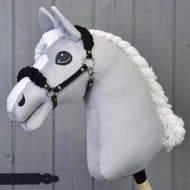 Schwarzes Halfter mit schwarzem Fell - Kunstleder von Hobby Horse LarDen an einem plüschigen hellgrauen Pferd mit schwarzem Halfter aus Kunstleder und großen aufgestickten Augen, vor grauem Holz Hintergrund.