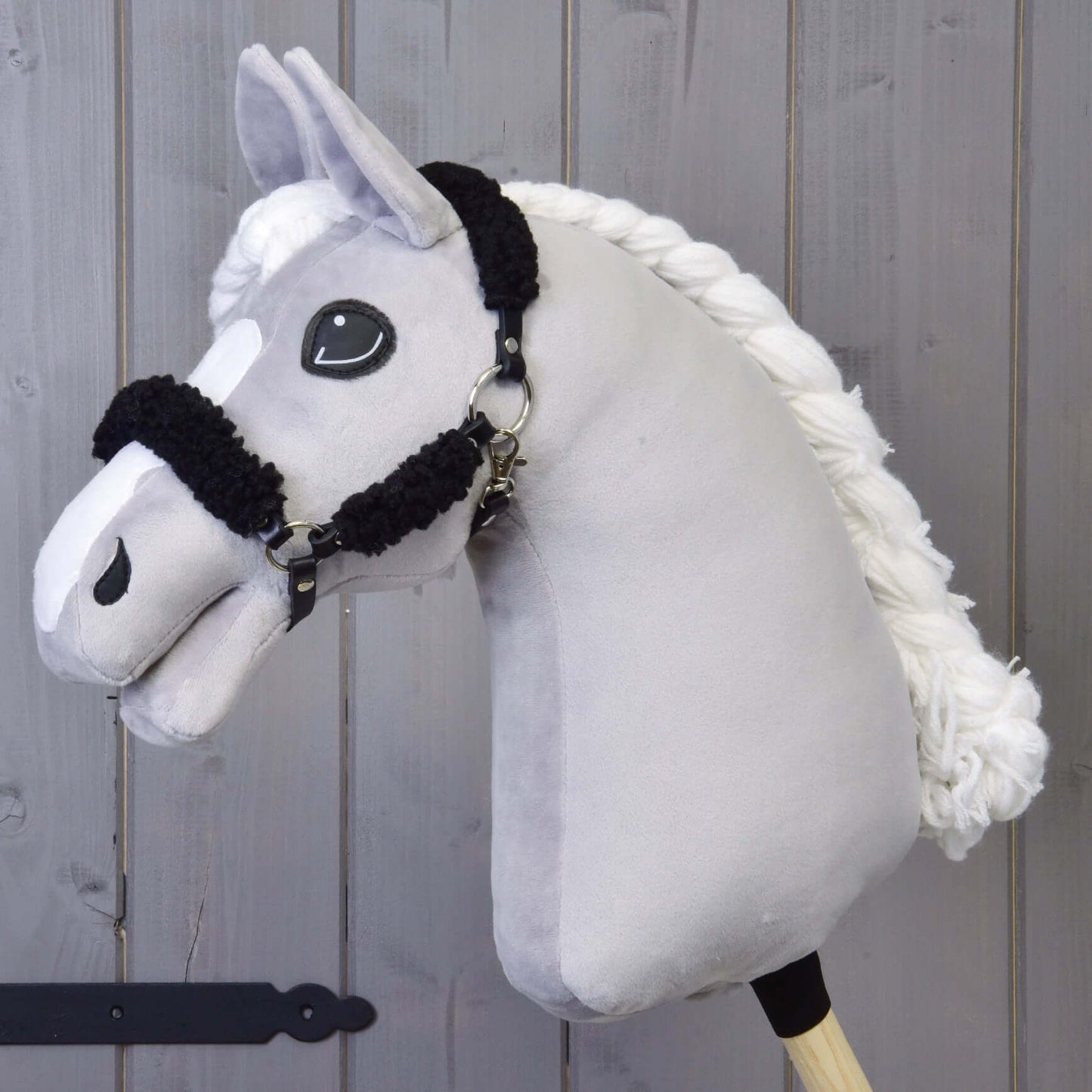 Licou noir avec fourrure noire complète - similicuir de Hobby Horse LarDen, présenté avec bâton en bois sur fond en panneaux de bois.