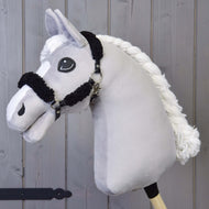 Hobby Horse LarDen mit Schwarzes Halfter mit Full Schwarzem Fell - Kunstleder und Holzstab, vor einem Hintergrund aus Holzpaneelen.