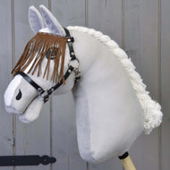 The Hobby Horse LarDen Halter Black with Brown Fringes features a plush hobby horse with a white mane and black harness, mounted on a wooden stick against a light gray wooden wall.