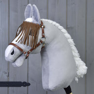 The Hobby Horse LarDen "Halter brown with fringes" is a plush hobby horse featuring a braided white mane, brown halter, and eye fringes, displayed in front of a gray wooden wall.