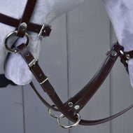 Nahaufnahme der Martingale braun von Hobby Horse LarDen mit braunem Lederzaumzeug mit Metallschnallen und -ringen an einem hellgrauen Modellpferdekopf, vor grauem Holz-Hintergrund.