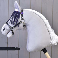 A close-up of the Hobby Horse LarDen toy featuring a gray body, white yarn mane, and a black halter with lila fringes, set against a wooden background.