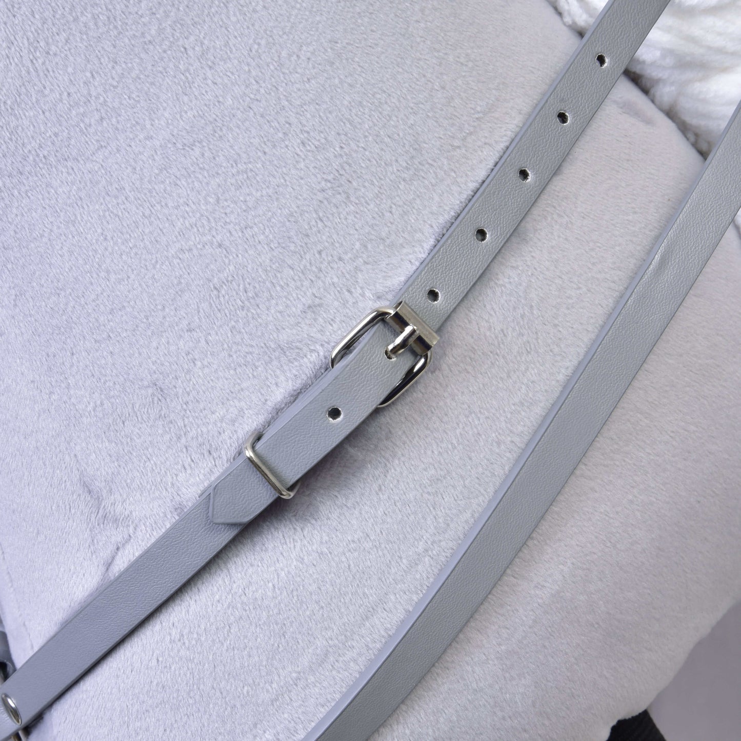 Gros plan de l’Ensemble gris en similicuir - bride, rênes et martingale de Hobby Horse LarDen, montrant la sangle gris clair avec boucle métallique sur un tissu gris pâle, idéal pour compléter votre harnachement de Hobby Horse.