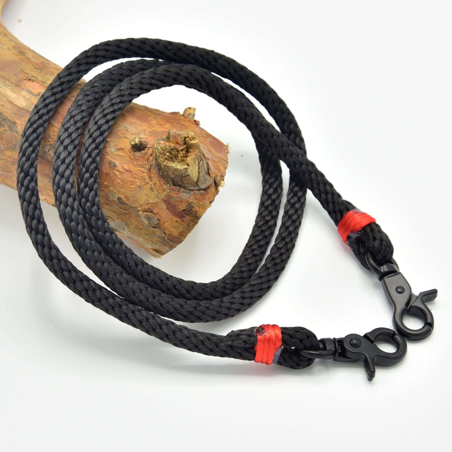 Rênes Étincelle de Hobby Horse LarDen en corde tressée noire en polypropylène avec mousquetons en métal aux deux extrémités et ligature rouge, enroulées sur une branche en bois, idéales comme rênes faites main ou rênes pour Hobby Horse.